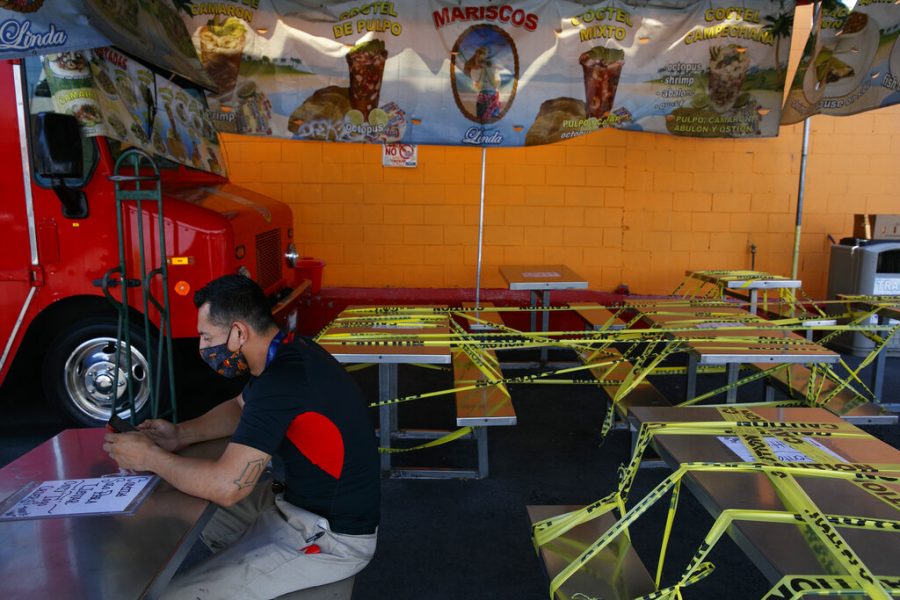 FILE - In this July 1, 2020, file photo, Abel Gomez waits for his order at Mariscos Linda food truck as dining tables are sealed off with caution tape due to the coronavirus pandemic in Los Angeles. Gov. Gavin Newsom announced a new, color-coded process Friday, Aug. 28, 2020, for reopening California businesses amid the coronovirus pandemic that is more gradual than the states current rules to guard against loosening restrictions too soon. Counties will move through the new, four-tier system based on their number of cases and percentage of positive tests. It will rely on those two metrics to determine a tier: case rates and the percentage of positive tests. (AP Photo/Jae C. Hong, File)