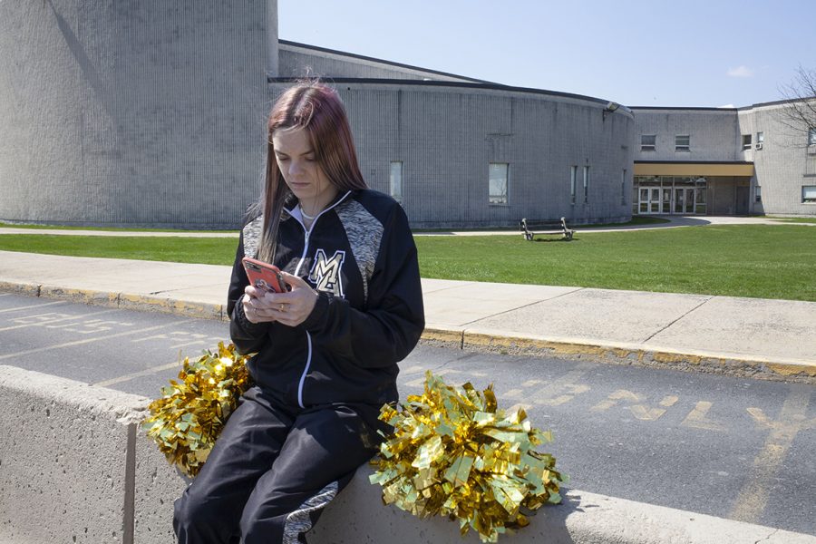 In this photo provided by the American Civil Liberties Union, Brandi Levy wears her former cheerleading outfit as she looks at her mobile phone while sitting outside Mahanoy Area High School in Mahanoy City, Pa., on April 4, 2021. A profanity-laced posting by Levy on Snapchat ​has ended up before the Supreme Court in the most significant case on student speech in more than 50 years. At issue in arguments to be heard Wednesday, April 28, 2021, via telephone, is whether public schools can discipline students over something they say off-campus. (Danna Singer/ACLU via AP)