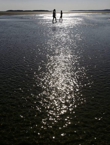Beach goers wade across a shallow part of Popham Beach as the ocean makes its way out during low tide on Monday, Oct. 10, 2011 in Phippsburg, Maine.  Another day of unseasonably warm temperatures treated people to a day at the beach. (AP Photo/Pat Wellenbach)